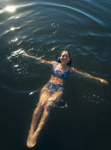 Model swimming in a lake wearing a black and white leopard print scoop neckline bikini top with under-bust band and adjustable straps with matching bottoms