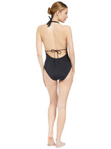 the back view of Model wearing black deep plunged one piece swimsuit with an adjustable halter-neck tie and under-bust string