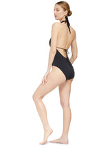 the side view of Model wearing black deep plunged one piece swimsuit with an adjustable halter-neck tie and under-bust string