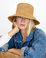 Woman wearing a straw hat and denim jacket against a white background