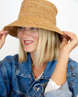 Woman wearing a straw hat and denim jacket on a plain background