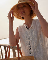 Woman wearing a straw hat and holding a woven bag on a beach.