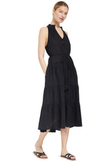 Model wearing a black sleeveless, high neck with ruffle detail, buttoned shirt dress with optional matching belt with tassels and hands in pockets. 