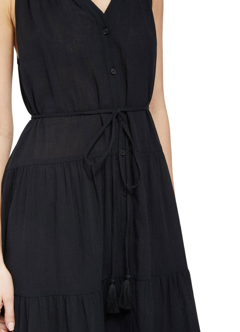 Close up and detailed shot of model wearing a black colored sleeveless, high neck with ruffle detail, buttoned shirt dress with optional matching belt with tassels