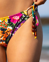 Colorful bikini bottom with floral pattern and beaded string on a blurred beach background