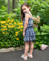 Young girl in a blue dress standing in a garden with flowers and greenery.