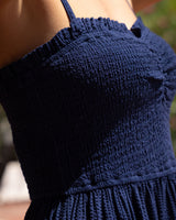 Close-up of a navy blue textured dress with a smocked bodice and thin straps, worn by a model in an outdoor setting.