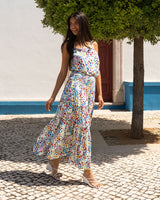 Woman in a floral dress standing under a tree on a sunny day.