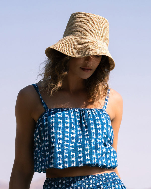 Woman wearing a blue patterned outfit and straw hat outdoors with a clear sky.