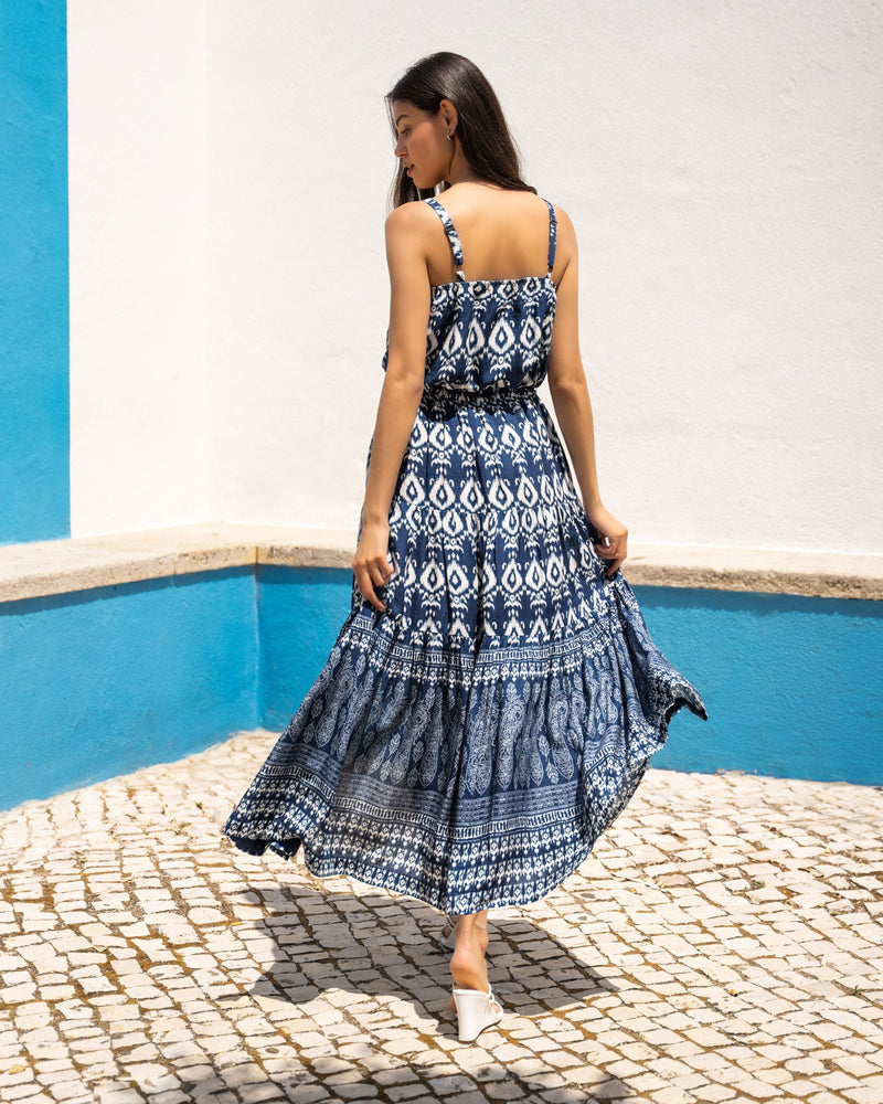 Woman in a blue patterned dress standing in front of a blue wall and pool.