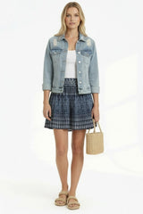 Woman wearing a denim jacket, white top, and plaid skirt with a straw bag on a white background