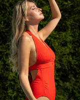 Woman in a red swimsuit standing against a green hedge
