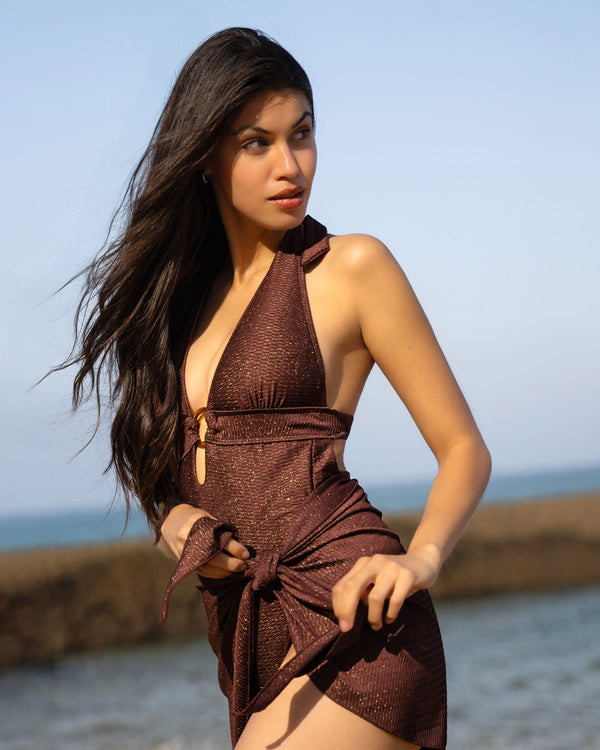 Woman in a brown dress standing by the ocean with a clear blue sky.