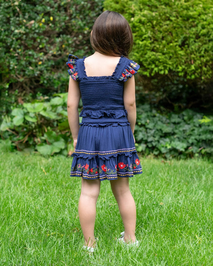Child wearing a blue dress with floral embroidery in a garden setting