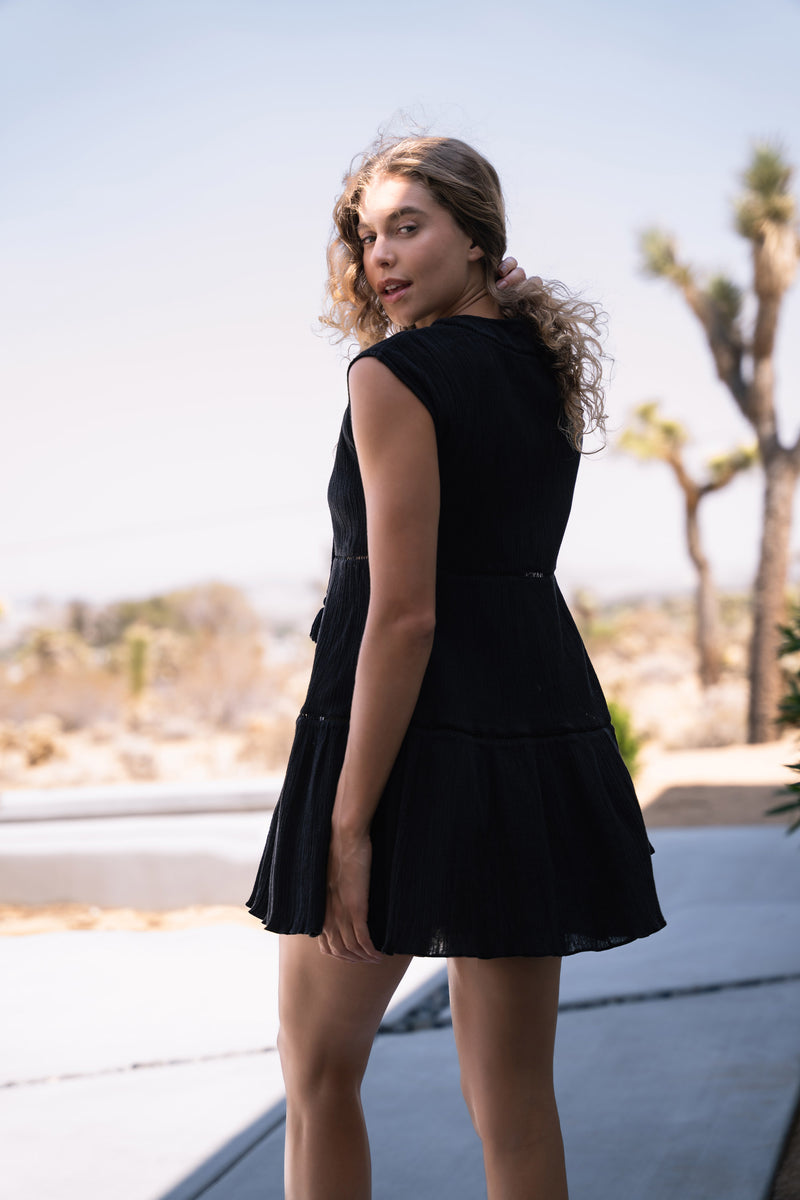 Woman in a black dress standing outdoors with desert landscape in the background