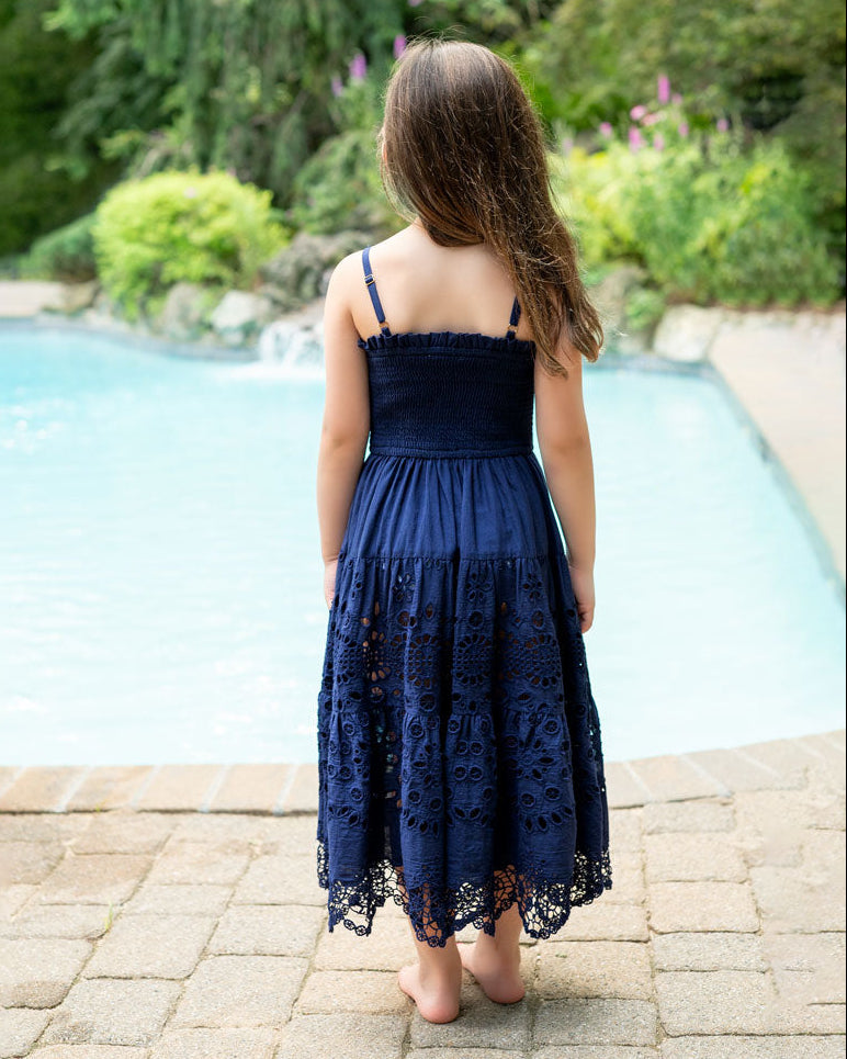Girl in a navy lace dress standing by a pool with greenery in the background