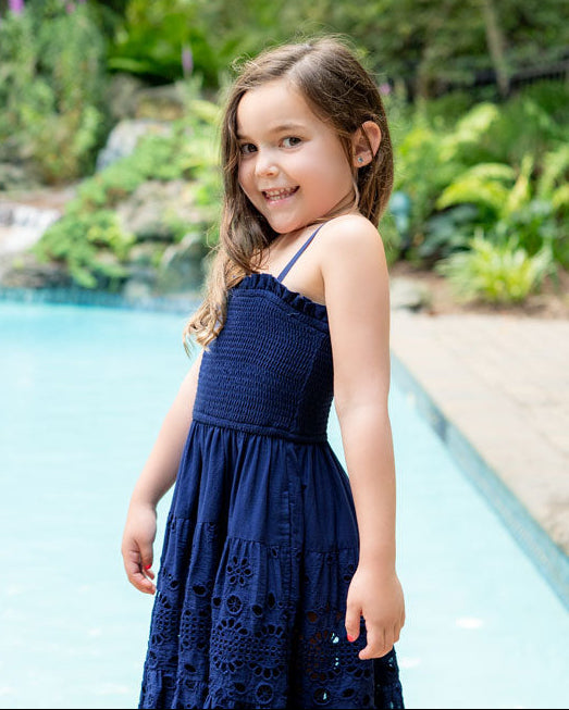 Young girl in a navy blue dress standing by a pool with greenery in the background
