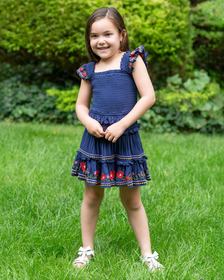 Young girl in a blue dress standing on grass with green bushes in the background