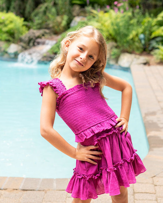 Young girl in a pink dress standing by a pool with a garden in the background