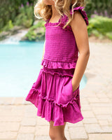 Child wearing a pink dress by a poolside with blurred greenery in the background