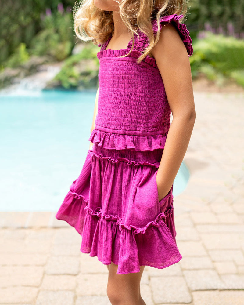 Child wearing a pink dress by a poolside with blurred greenery in the background