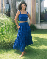 Woman in a blue outfit standing outdoors on grass with plants and a building in the background