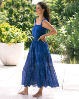 Woman in a blue dress standing outdoors with greenery in the background