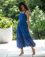 Woman in a blue lace dress standing outdoors with greenery in the background