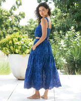 Woman in a blue lace dress standing outdoors with greenery in the background