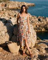 Woman in a floral dress standing on rocky terrain by the sea