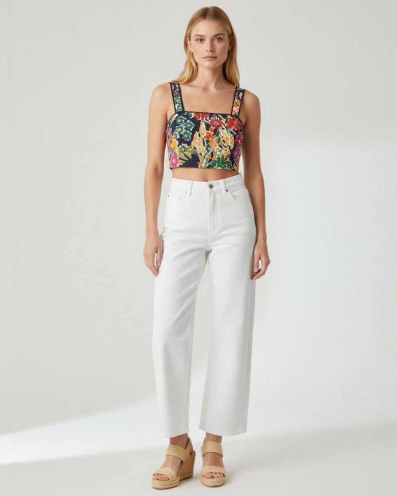 Woman wearing a floral crop top and white pants on a white background