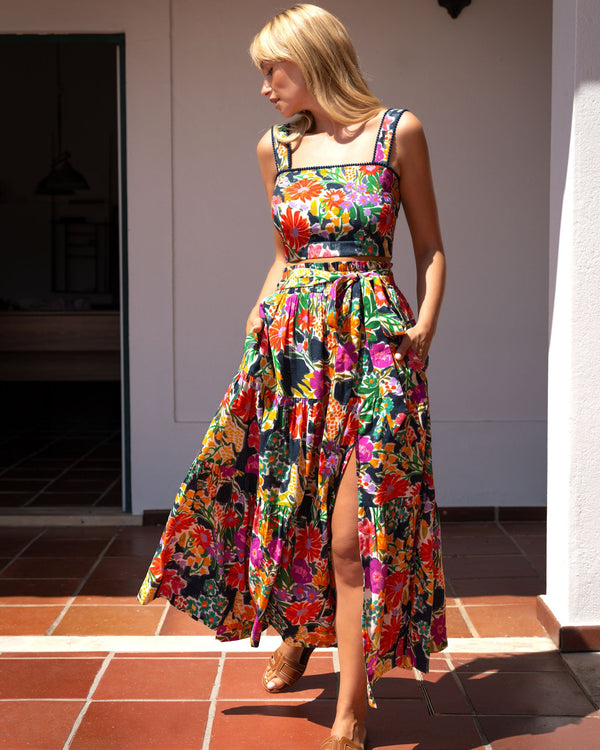 Woman wearing a colorful floral dress standing on a tiled patio.