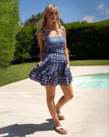 Woman in a blue patterned dress standing by a pool with greenery in the background