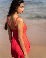 Woman in a red dress standing on a beach with ocean in the background