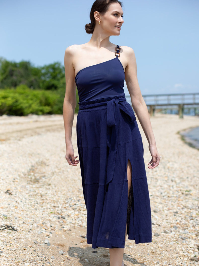 Closer shot of model with head turned to ocean wearing navy one shoulder strap one piece bathing suit