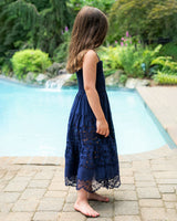Girl in a navy blue lace dress standing by a poolside with greenery in the background