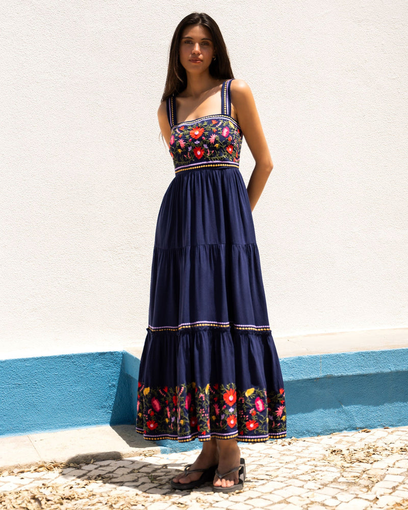 Woman wearing a navy blue dress with floral patterns standing on a stone path.