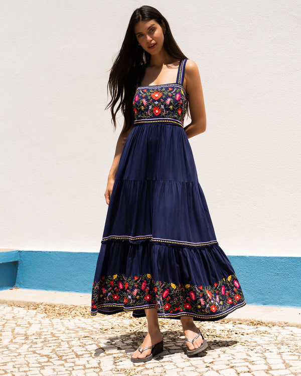 Woman wearing a navy blue dress with floral embroidery on a white wall background