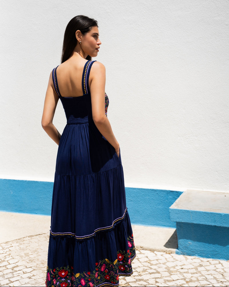 Woman wearing a navy blue dress with floral details, standing against a white wall with blue accents.