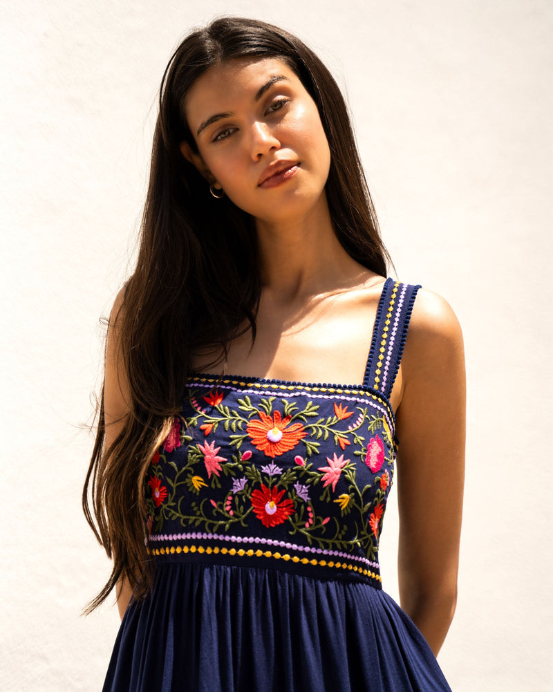 Woman wearing a navy blue dress with colorful floral embroidery against a plain background