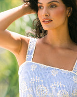 Woman wearing a blue and white striped dress with floral embroidery, standing outdoors.