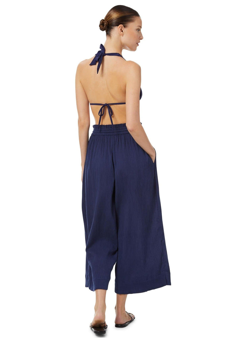 The back of a model wearing navy blue organic cotton beach pants with elastic waistband with drawstring and tassel detail with matching navy lye triangle bikini top 