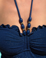Close-up of a blue bikini top with a necklace featuring blue beads and gold accents.