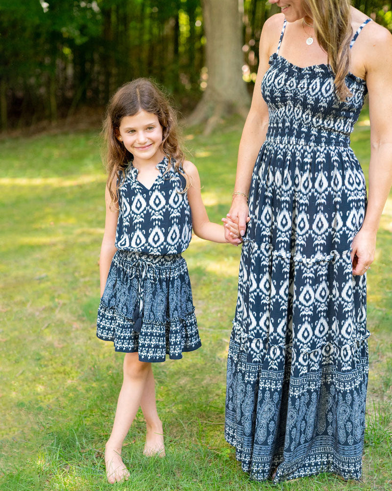 Mom and daughter wearing matching blue and white patterned dresses standing outdoors on grass.