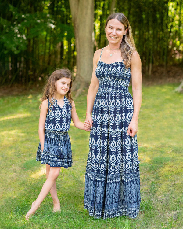 Mom and daughter wearing matching blue patterned dresses standing outdoors.