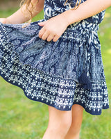 Young girl wearing a blue and white patterned dress outdoors on a sunny day.