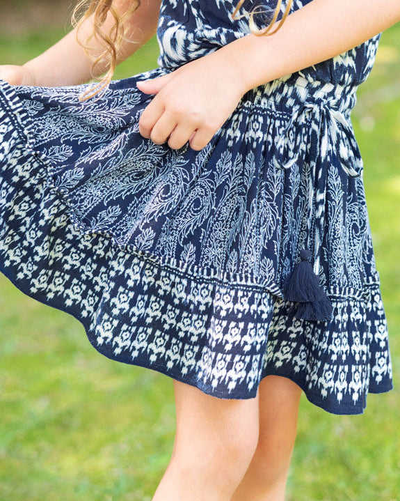 Young girl wearing a blue and white patterned dress outdoors on a sunny day.