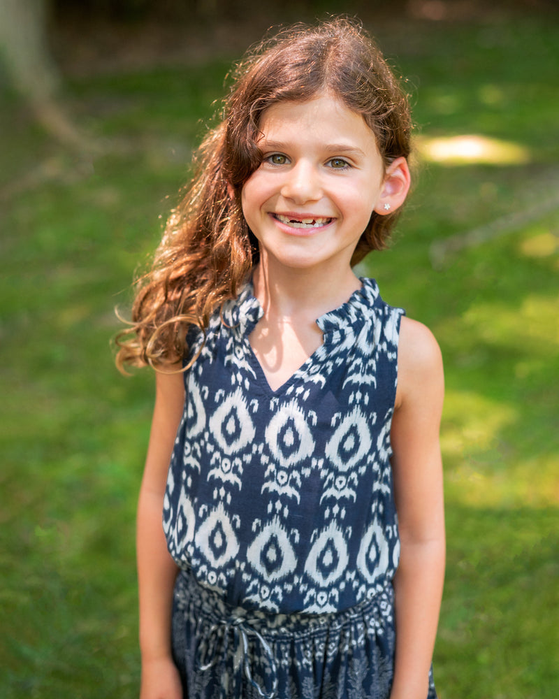 Young girl wearing a blue patterned dress standing outdoors with green grass in the background