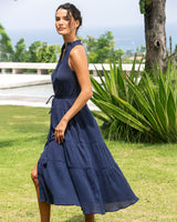 Woman in a navy blue dress standing outdoors with greenery and water in the background