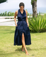 Woman wearing a navy blue dress standing on grass with greenery in the background